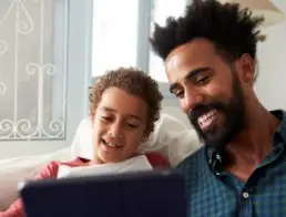Father and son using a tablet together on their couch